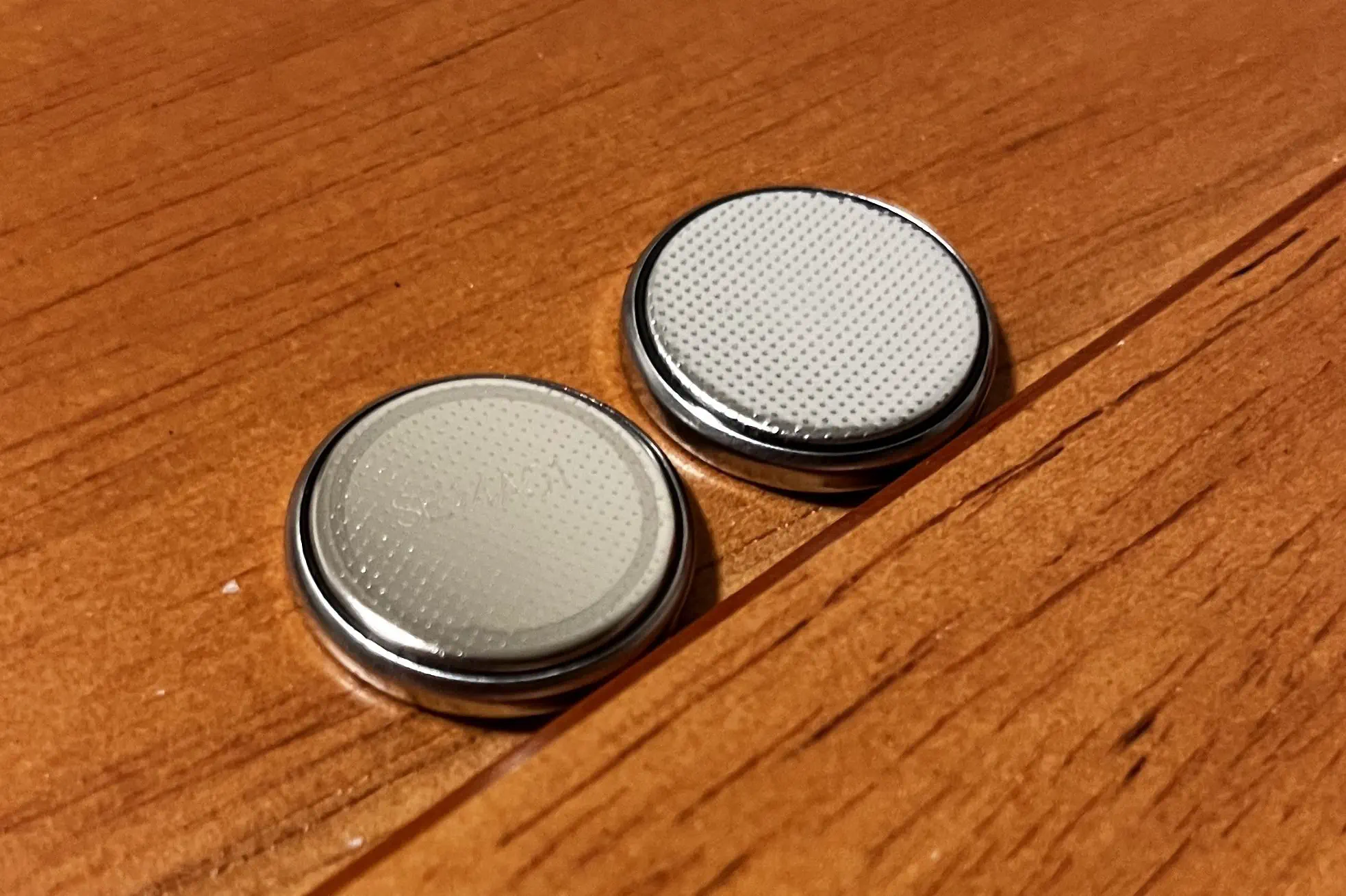Two CR2023 batteries, bottom side up. The left one has fade outlined ring around the edges, while the one on the right does not.